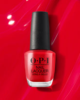 OPI nail polish bottle of Red Heads Ahead nail lacquer standing upright against a glossy red background, showcasing the bold bright red shade in a clear glass bottle with black cap for a vibrant manicure look.