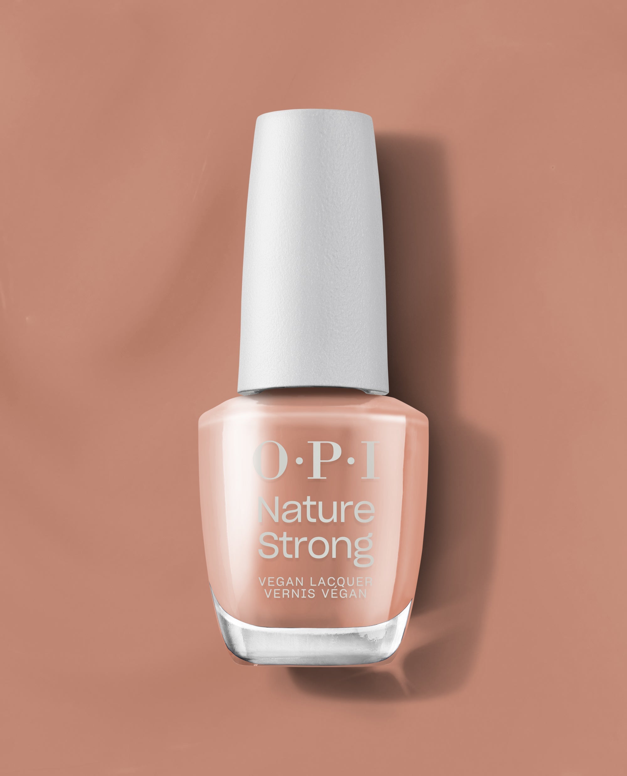 OPI Nature Strong Vegan Nail Lacquer in Rooting For Hue, a trending peachy nude nail polish with a white cap, standing on a warm terracotta background.