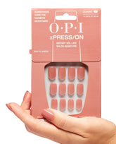 Hand holds OPI Somewhere Over the Rainbow Mountains xPRESS/ON Iconic Shades short press on nails, showing peachy nude glossy tips in a pink box, ideal as an OPI nail polish gift set for an instant gel-like salon manicure at home.