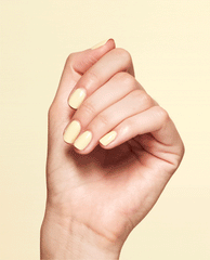 Hand with glossy pale yellow nails showcasing OPI Blinded by the Ring Light Nail Lacquer against a soft yellow background.