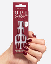 A hand with glossy deep burgundy nails holds OPI On Point Como se Llama? instant press-on mani pack, showing matching square nails and up to 14 days wear on a white studio background, ideal for fall nail colors.