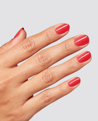 Hand shows glossy coral-red Special O-Cajun at-home gel nail polish on short rounded nails against a light gray background, a trending OPI-inspired manicure shade.
