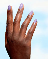 Hand displays glossy lavender OPI Spring Into Action Nature Strong vegan nail lacquer on almond-shaped nails against a soft blue background, a fresh pick for fall nail colors.
