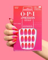 Hand with glossy pink-to-orange ombré almond nails holds the trending OPI xPRESS/ON Squeeze the Day press-on nail kit, showing matching gel-like nails in bright pink packaging.