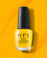 OPI Sun, Sea, and Sand in My Pants nail lacquer stands upright, displaying a bold marigold-yellow polish with a black cap on a matching sunny backdrop, spotlighting spring nail colors and spring nail trends for a vibrant US manicure.