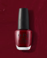OPI We the Female nail lacquer bottle stands upright, showing a deep red polish shade against a matching glossy red background, ideal for rich fall nail colors.