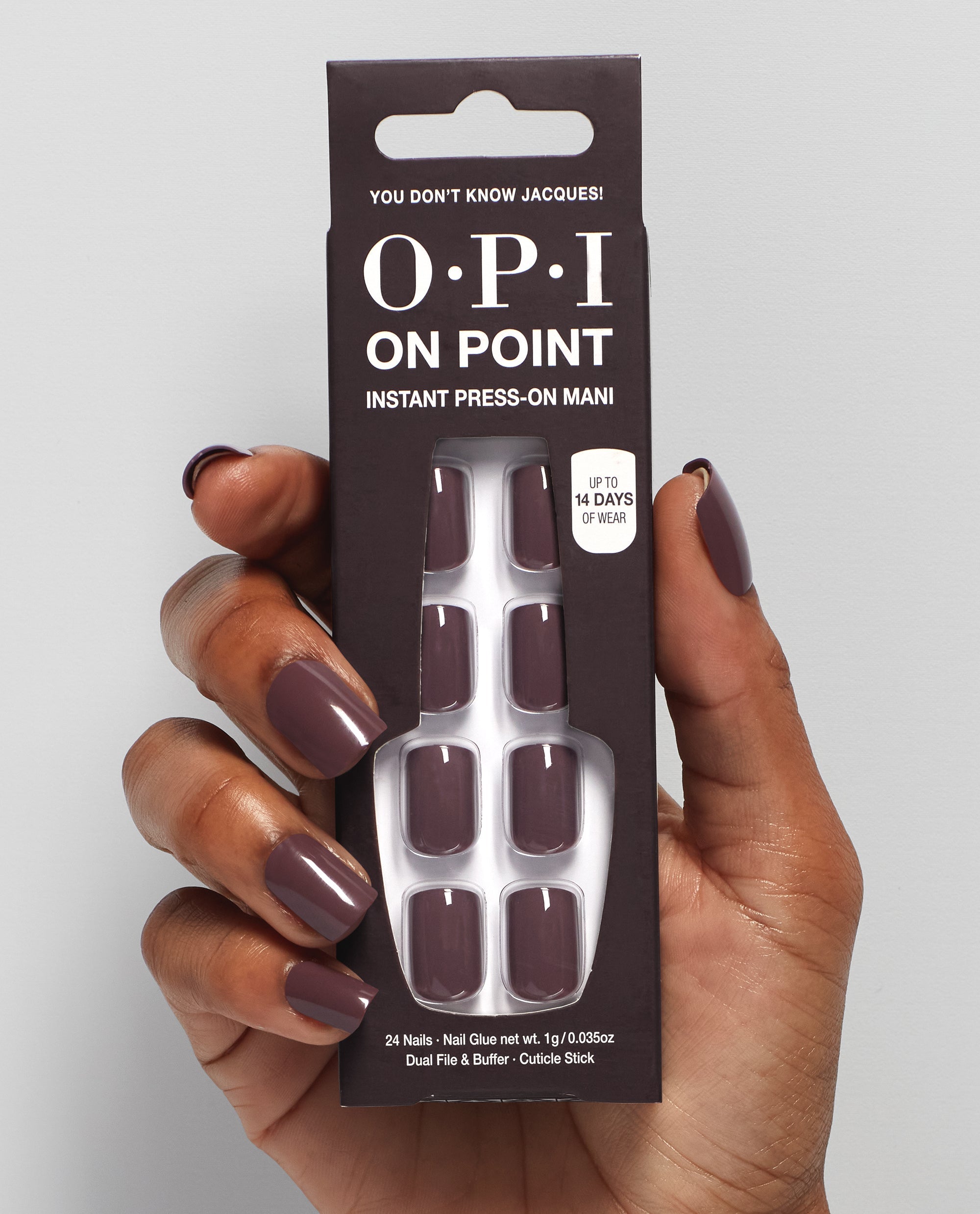 Hand with glossy taupe-mauve OPI On Point press-on nails holds the You Don’t Know Jacques! instant press-on mani box, showing matching nails and 14-day wear claim on a light gray studio background, ideal for fall nail colors.