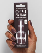 Hand with glossy taupe-mauve OPI On Point press-on nails holds the You Don’t Know Jacques! instant press-on mani box, showing matching nails and 14-day wear claim on a light gray studio background, ideal for fall nail colors.