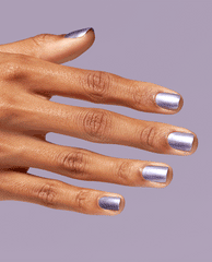Hand with short, neatly manicured nails painted in OPI nail polish shade You’ve Got Nail, a shimmery metallic lavender nail lacquer, held against a matching pastel purple background for a modern, polished look.