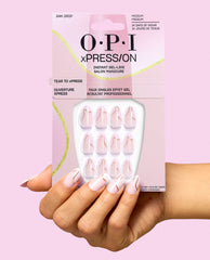 OPI 24K Drip xPRESS/ON medium press-on nails in pale pink with gold swirl accents, held in matching packaging against a pink background for chic fall nail colors.