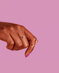 Hand wearing delicate gold rings shows glossy magenta 7th & Flower nail lacquer, with the OPI nail polish shade shining against a solid pink background in a close-up beauty product shot.