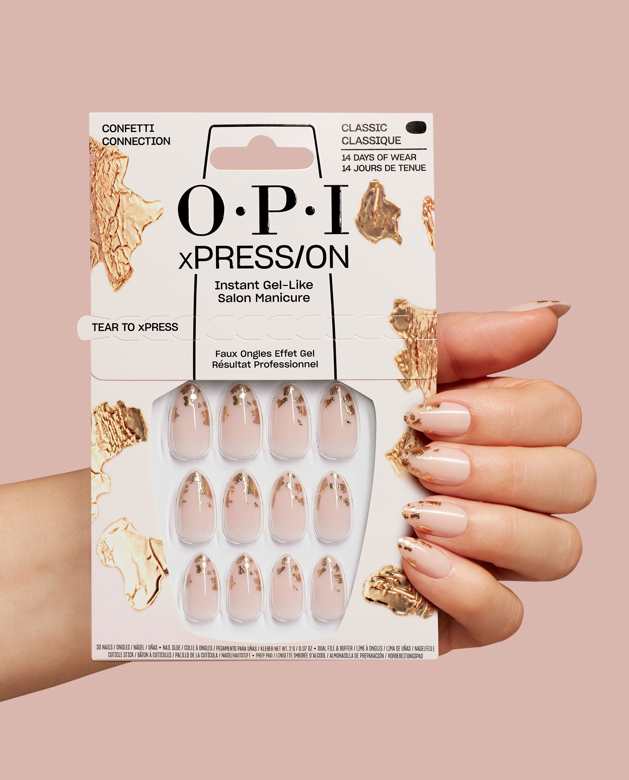 Hand holds OPI Confetti Connection xPRESS/ON nail art kit, showing nude press-on nails with gold foil accents in retail packaging against a blush background, styled as a chic OPI nail polish gift set for salon-quality manicures at home.