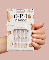 Hand holds OPI Confetti Connection xPRESS/ON nail art kit, showing nude press-on nails with gold foil accents in retail packaging against a blush background, styled as a chic OPI nail polish gift set for salon-quality manicures at home.