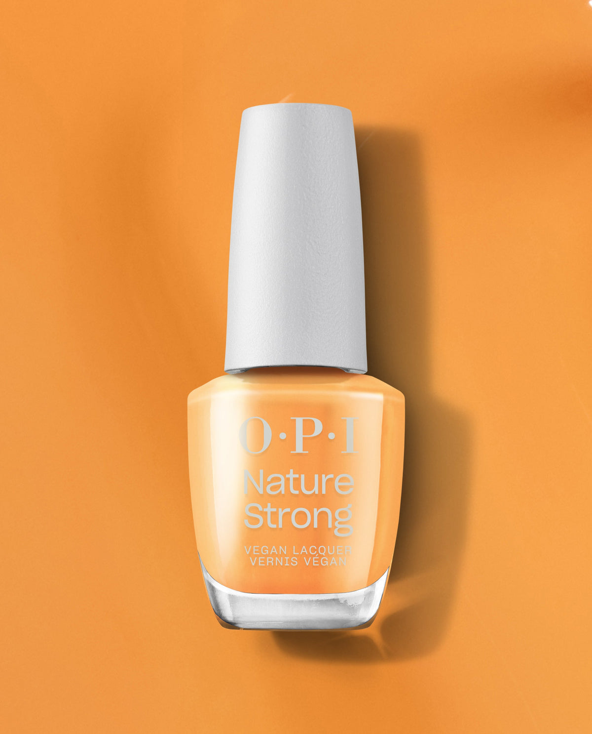 OPI Nature Strong Bee the Change vegan nail lacquer stands upright, showcasing its honey-gold creme shade against a matching amber backdrop - an eco-conscious pick for spring nail colors and spring nail trends from OPI.