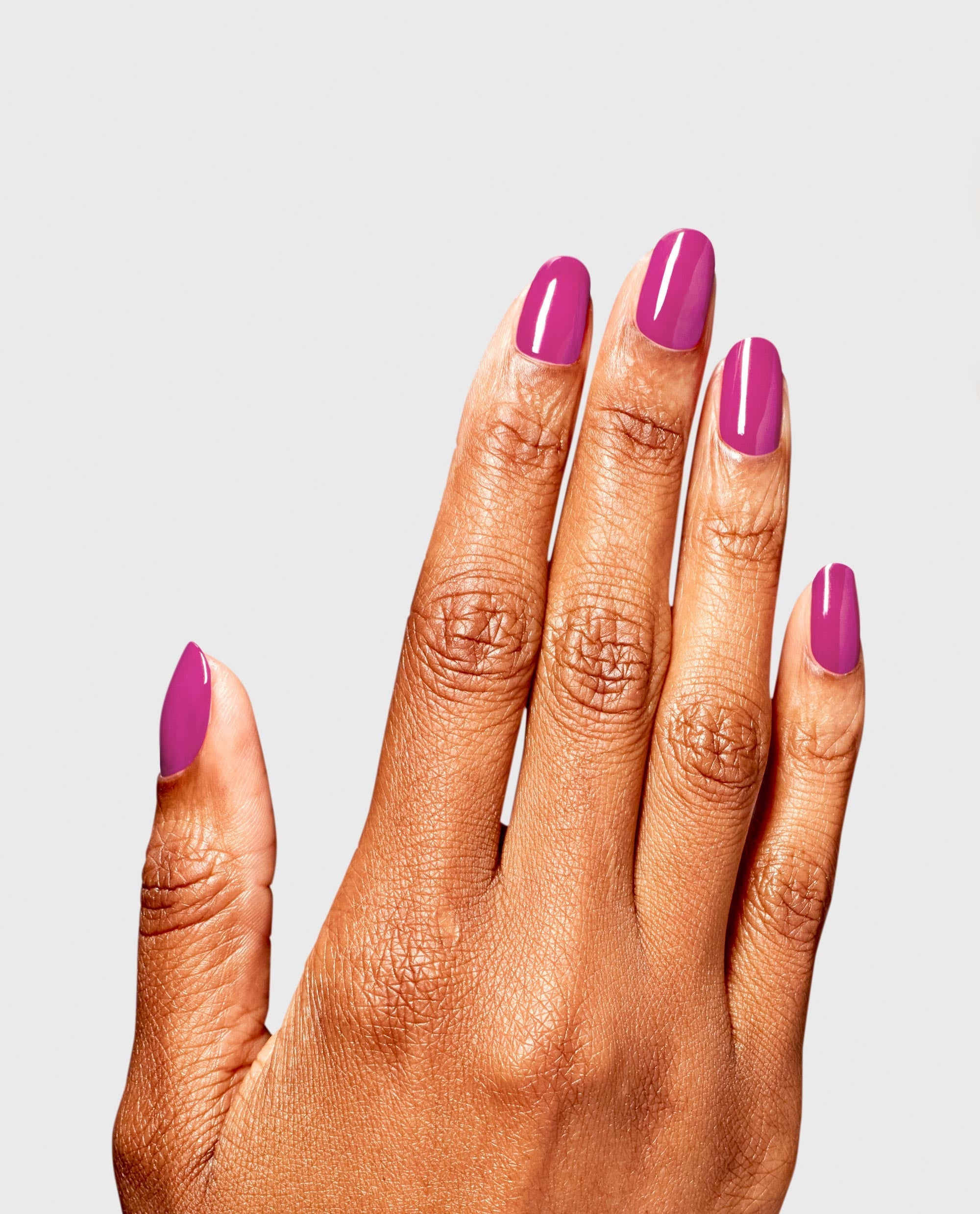 Hand with neatly manicured nails showcases OPI ASAPink RapiDry nail polish gift set shade, a glossy vibrant pink, against a clean light gray background for a modern beauty product display.