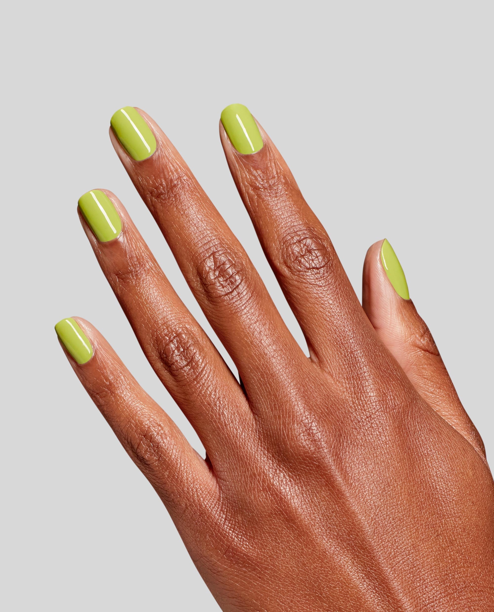 Lime-green manicure on a splayed hand, showcasing OPI Screen-Grab Green RapiDry™ green nail polish with a glossy shine against a plain gray background, highlighting trending spring nail colors.