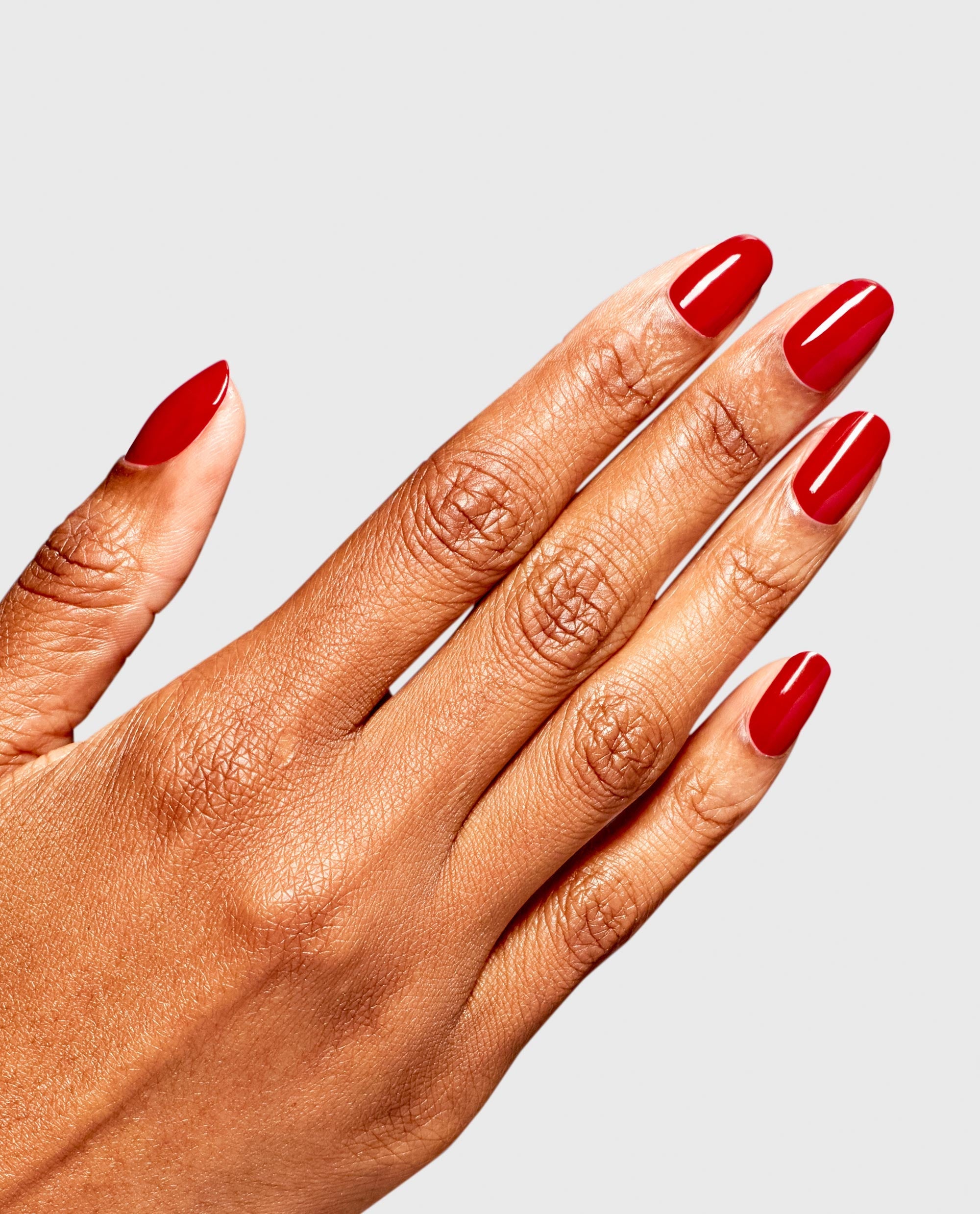 Hand displays glossy almond-shaped nails in OPI RapiDry Secs Appeal, a rich red shade for fall nail colors, against a clean light gray background.