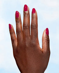 Hand showing glossy berry-red nails painted with OPI A Bloom with a View Nature Strong Vegan Nail Lacquer, a rich shade for fall nail colors, against a pale blue background.