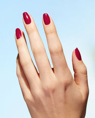 Hand showcasing glossy deep berry nails painted with OPI A Bloom with a View Nature Strong vegan nail lacquer, a rich shade for fall nail colors on a light blue background.