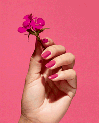 A Kick in the Bud Nature Strong Vegan Nail Lacquer by OPI coats glossy fuchsia nails as a hand holds a small pink flower, highlighting vibrant spring nail colors and spring nail trends against a matching pink backdrop.