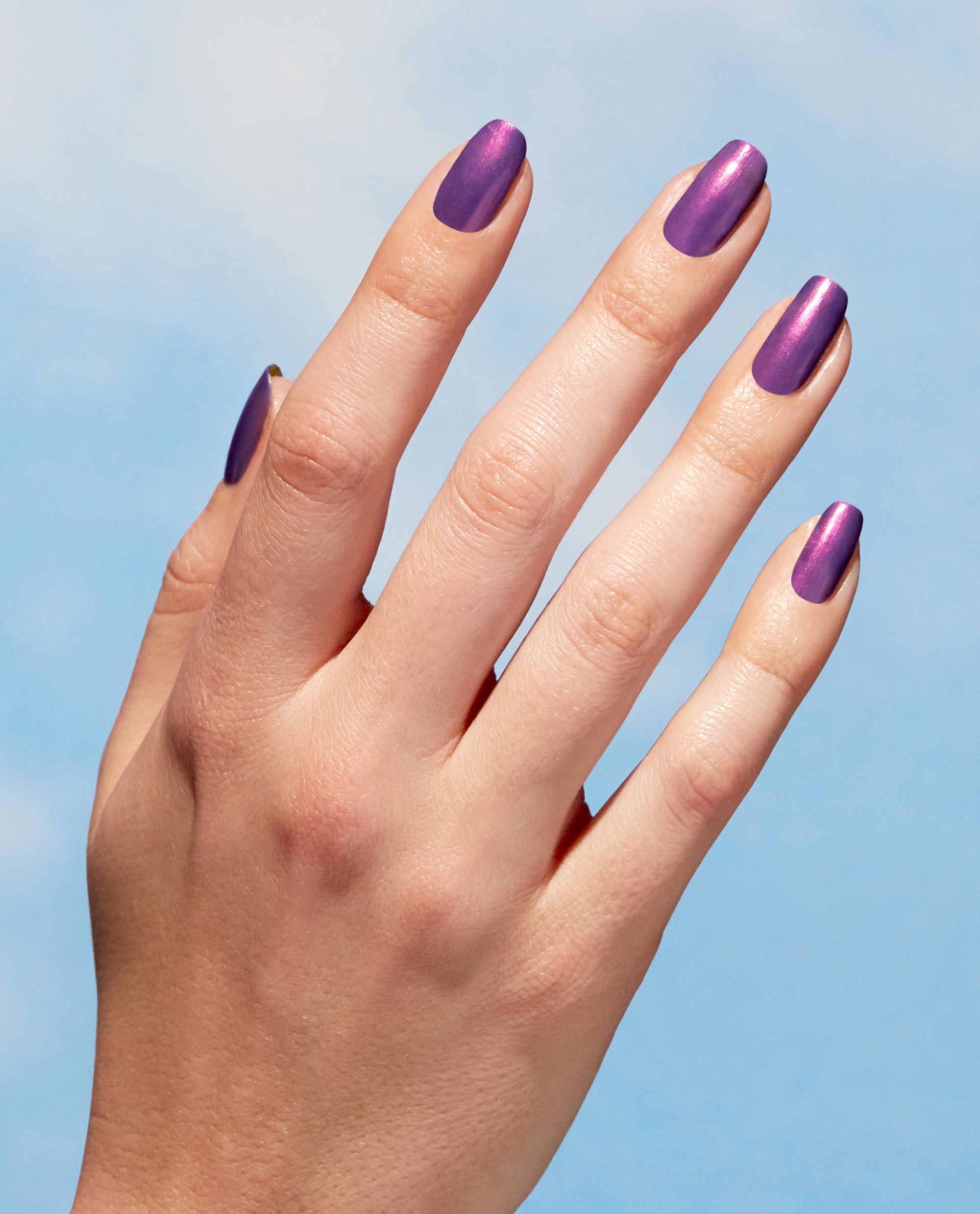 Hand models OPI Nature Strong Vegan Nail Lacquer in Achieve Grapeness, a shimmering purple shade for fall nail colors, against a soft blue background.