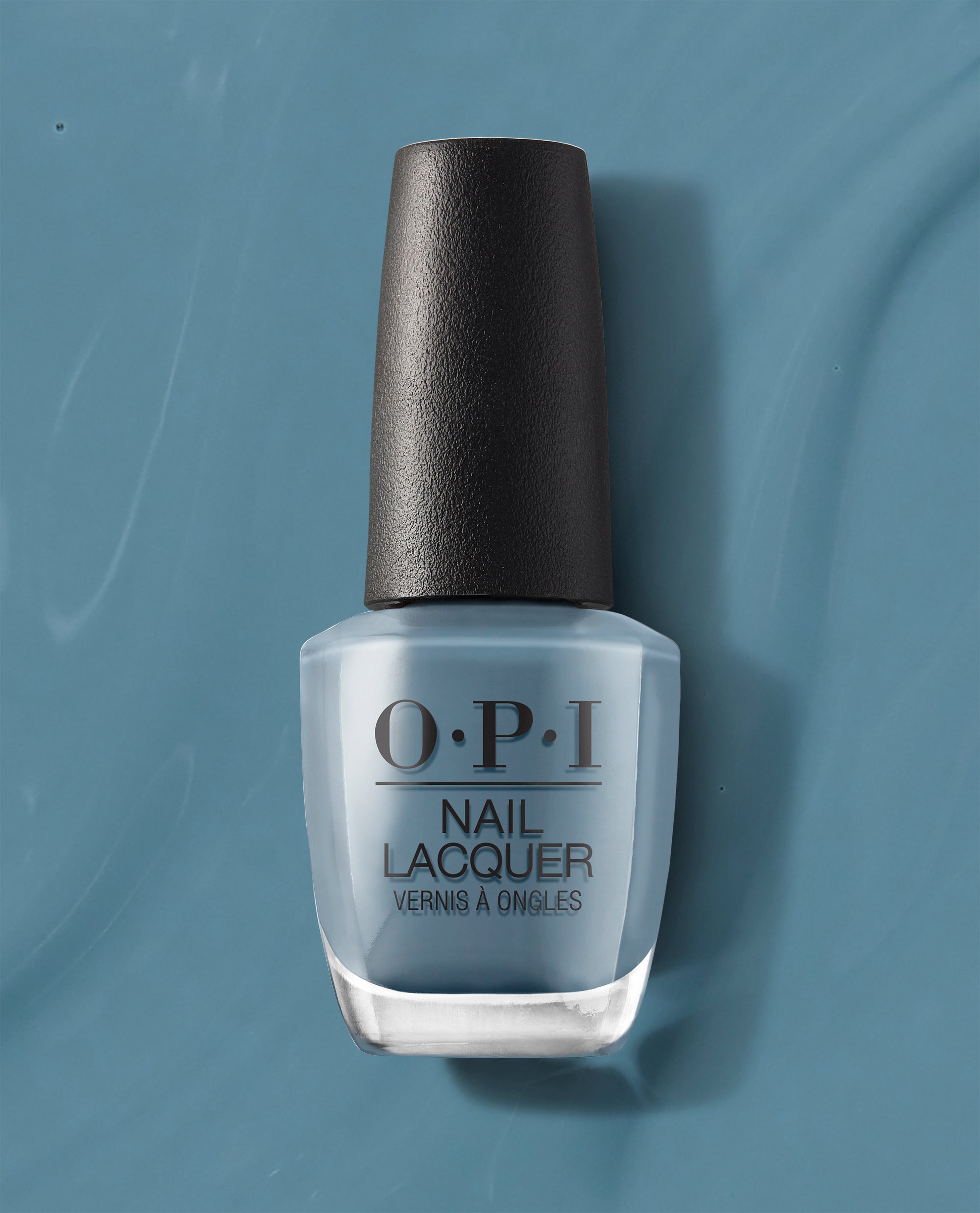 OPI Alpaca My Bags Nail Lacquer bottle showcasing a muted dusty blue with gray undertones, standing upright against a coordinating teal-blue background, perfect for cool-toned fall nails.