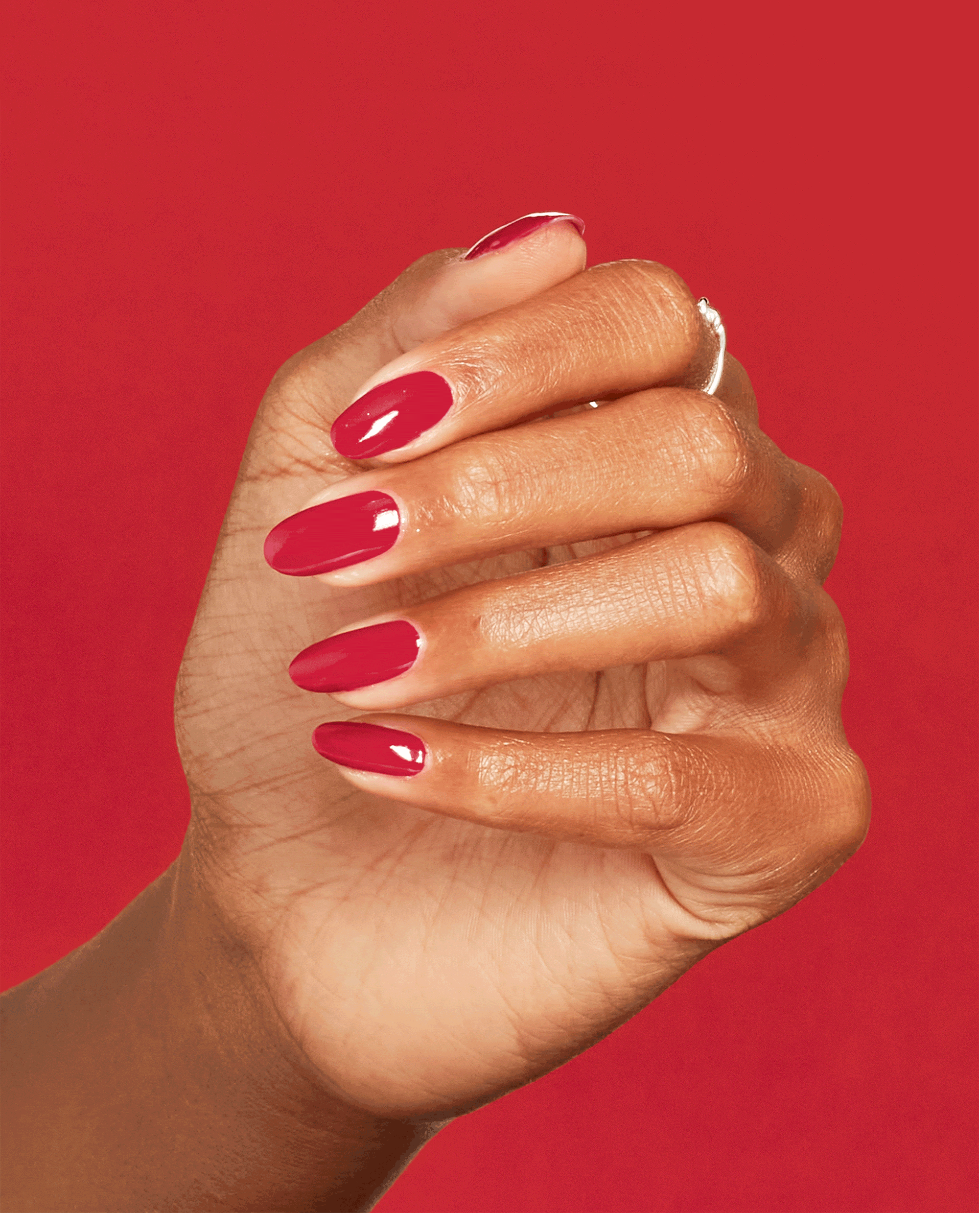 Hand with medium skin tone flexing fingers to showcase glossy crimson nails painted with Art Walk in Suzi's Shoes OPI nail polish nail lacquer against a bold red background, highlighting the smooth, even salon-quality manicure finish.