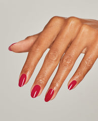 Woman’s hand displaying glossy medium-length nails painted in Art Walk in Suzi’s Shoes, a vibrant pink-red OPI nail polish nail lacquer, against a plain light gray background, highlighting the smooth, even, high-shine manicure finish.