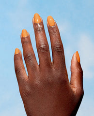 Hand showcases glossy Bee the Change manicure, a sunny marigold‑orange creme from OPI Nature Strong Vegan Nail Lacquer, shining against a clear blue sky - perfect for spring nail colors and spring nail trends from OPI.