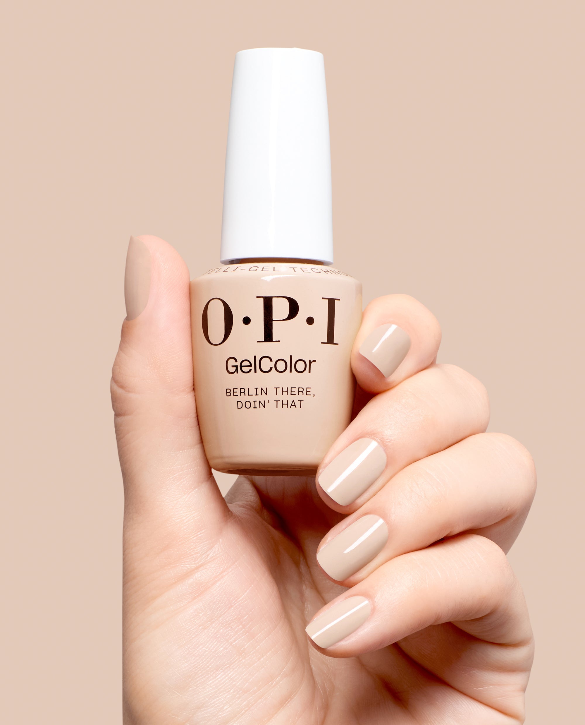 Hand holding OPI GelColor Berlin There, Doin’ That gel nail polish in a glossy beige-taupe shade, with matching manicured nails against a soft neutral background for fall nail colors.