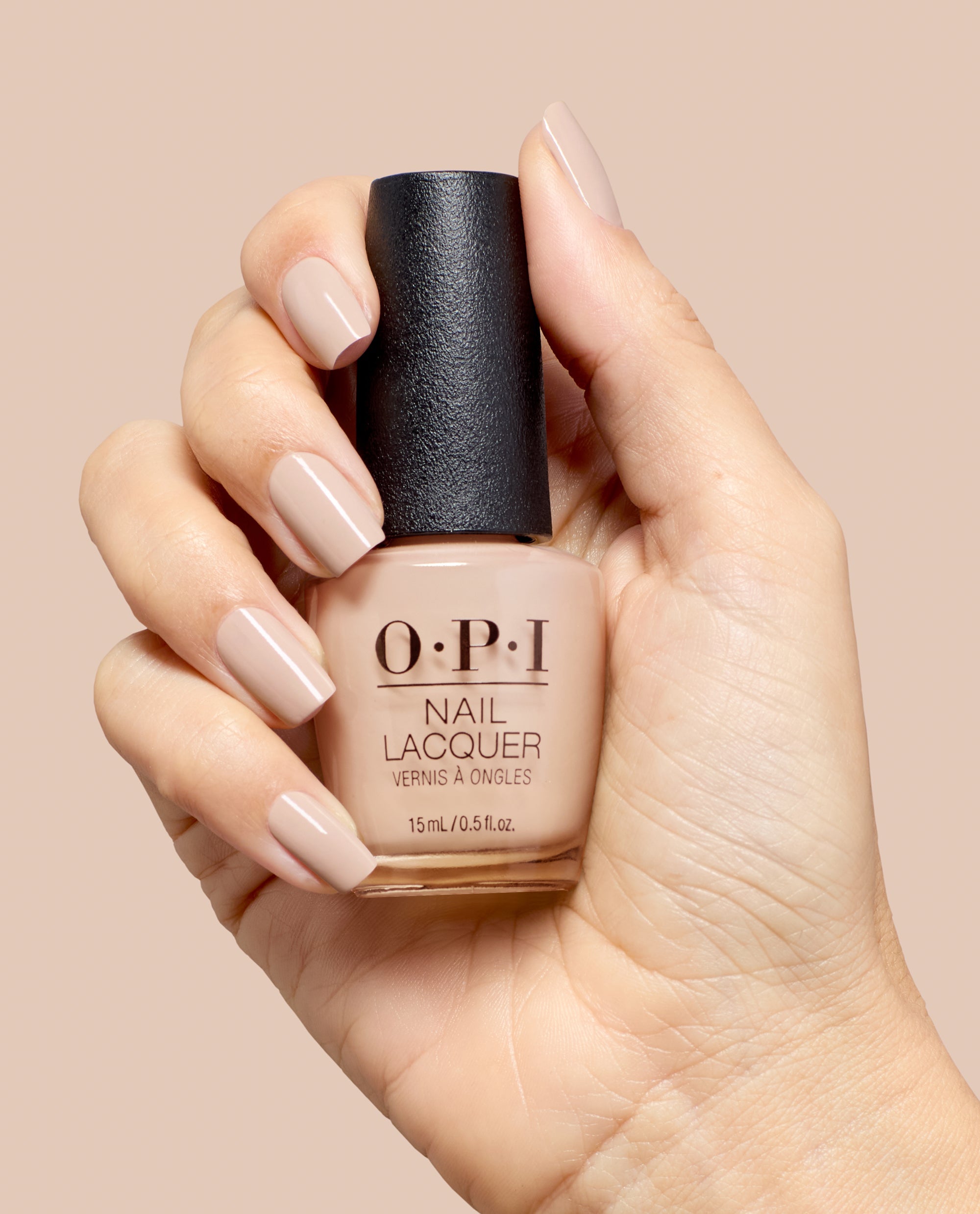 Hand holds OPI Berlin There, Doin’ That nail lacquer, showing glossy taupe-beige nails and matching bottle shade against a soft nude background, ideal for fall nail colors.