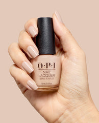 Hand holds OPI Berlin There, Doin’ That nail lacquer, showing glossy taupe-beige nails and matching bottle shade against a soft nude background, ideal for fall nail colors.