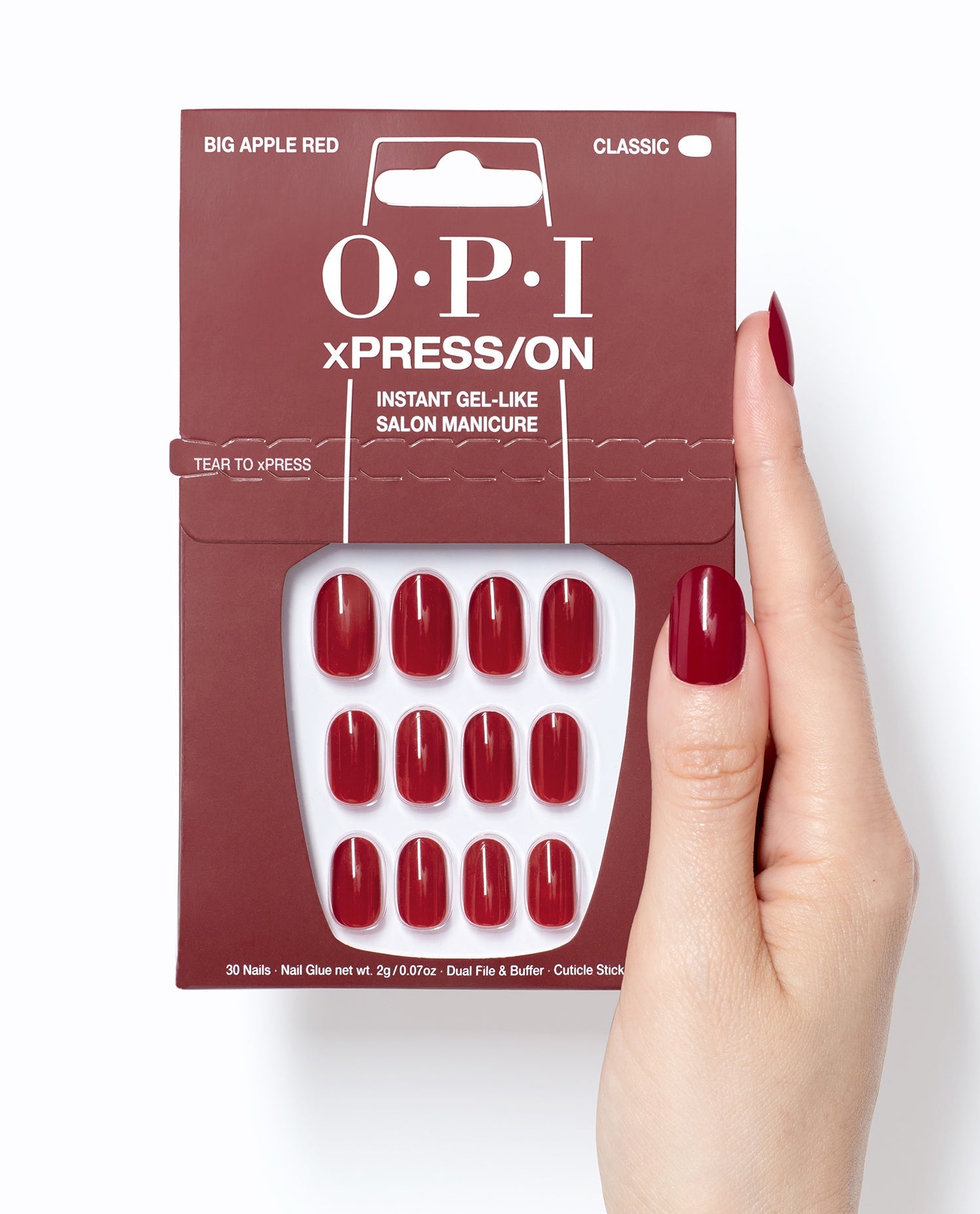 OPI Big Apple Red xPRESS/ON press-on nails in glossy classic red shown in retail packaging beside a hand wearing matching gel-like manicure nails on a white background.