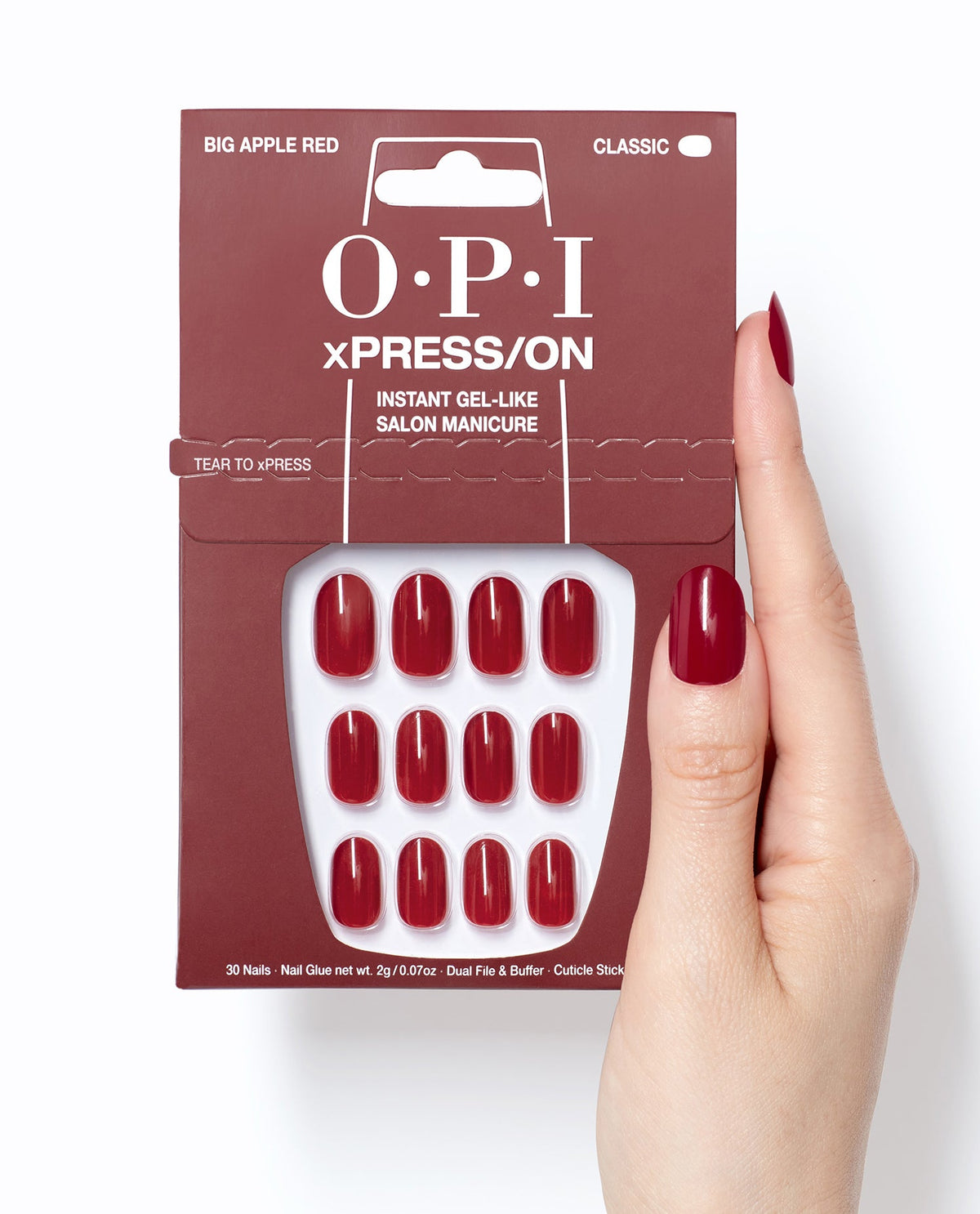 OPI Big Apple Red xPRESS/ON press-on nails in glossy classic red shown in retail packaging beside a hand wearing matching gel-like manicure nails on a white background.