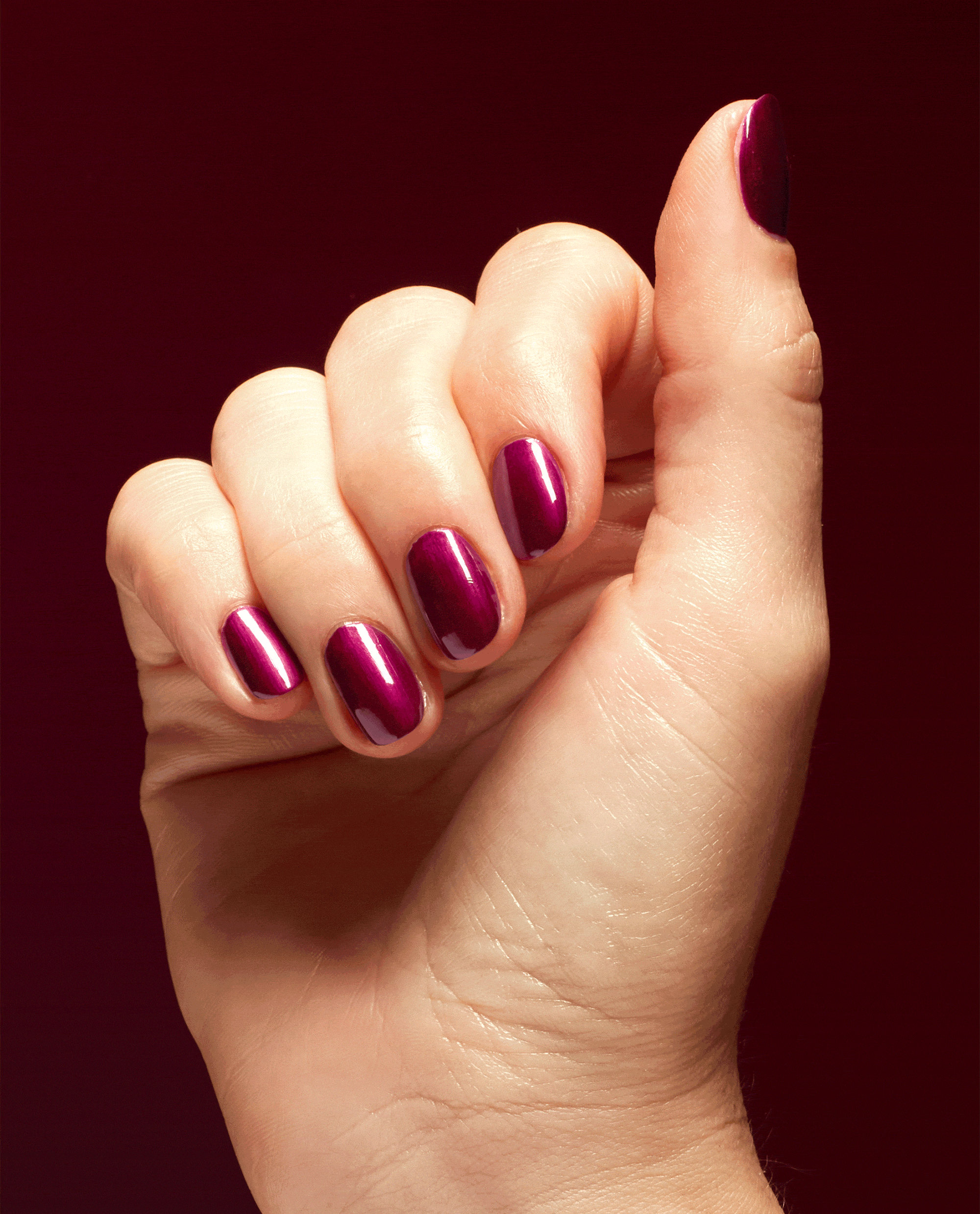Hand showing short, rounded nails painted in Big Sagittarius Energy, a deep shimmery magenta OPI nail polish, catching the light against a rich burgundy background for a bold, glossy manicure look.