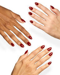 Hands with diverse skin tones display glossy almond-shaped OPI xPRESS/ON nails in Big Apple Red, a deep red shade for classic fall nail colors, on a clean white background.