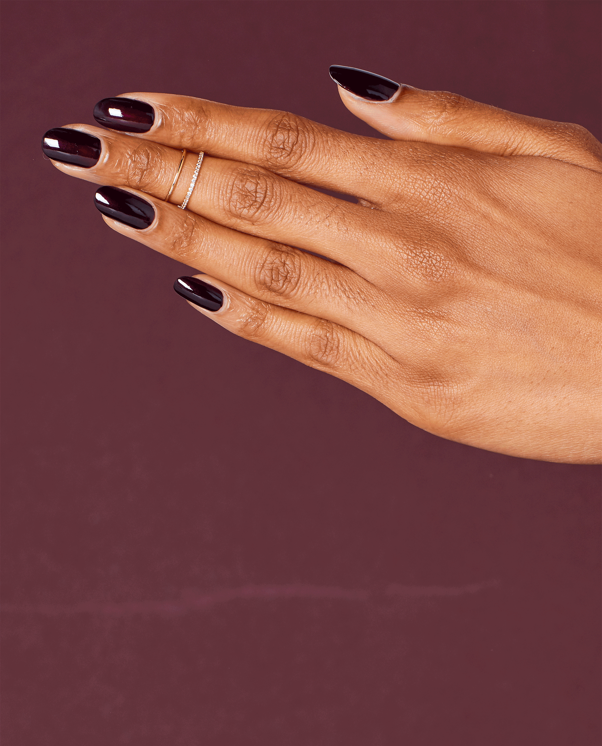 Hand modeling glossy OPI Black Cherry Chutney nail lacquer, a deep black cherry shade for fall nail colors, against a rich burgundy background.