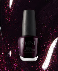 OPI Black Cherry Chutney nail lacquer bottle in deep blackened plum stands against a shimmering burgundy glitter background, a rich choice for fall nail colors.