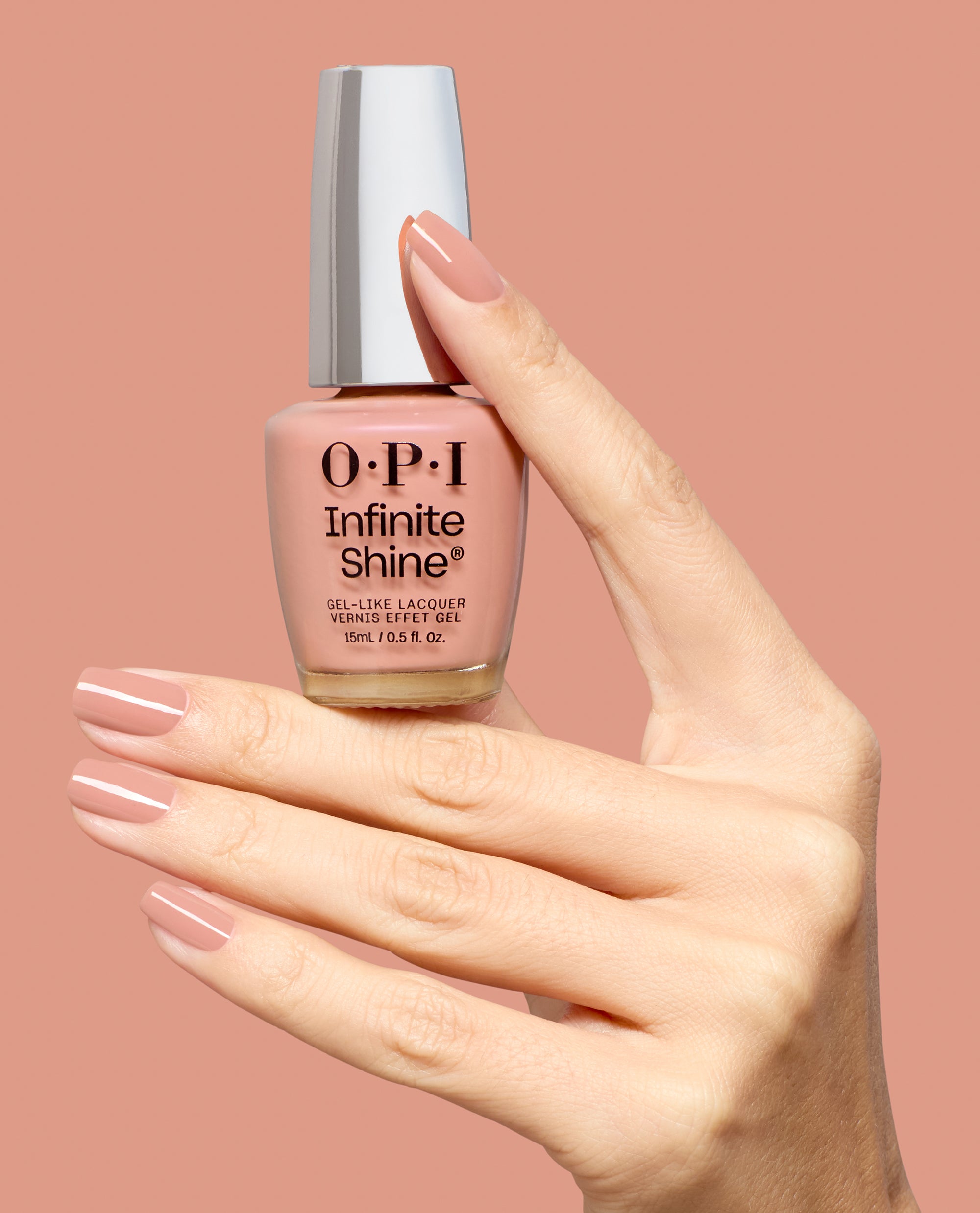Hand with glossy mauve-pink nails holds OPI Infinite Shine Boots in Barcelona gel-like lacquer bottle against a matching pink background, showcasing fall nail colors.