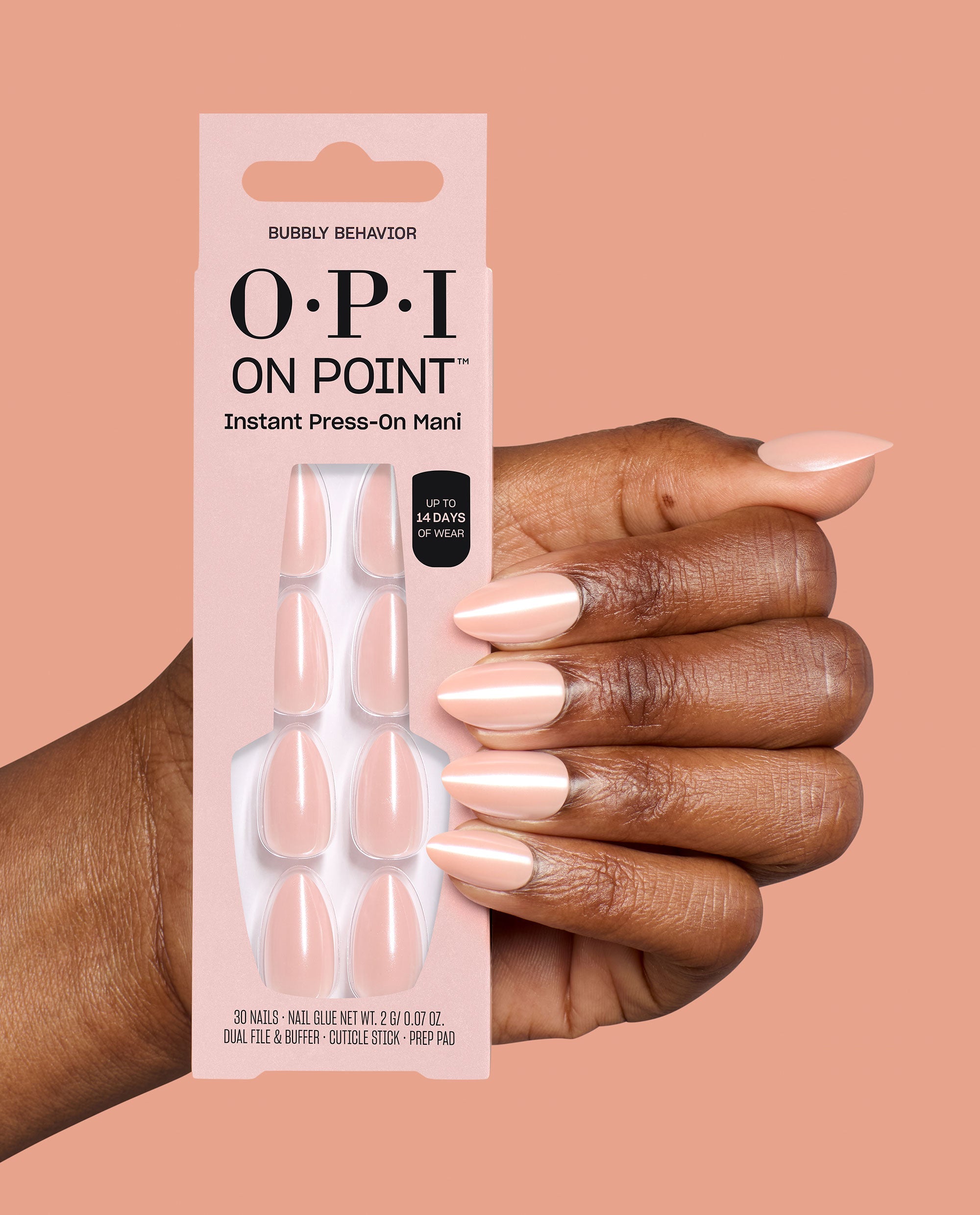 Hand wearing pale pink almond press-on nails holds OPI On Point Bubbly Behavior Instant Press-On Mani packaging, a soft neutral option for fall nail colors on a peach background.