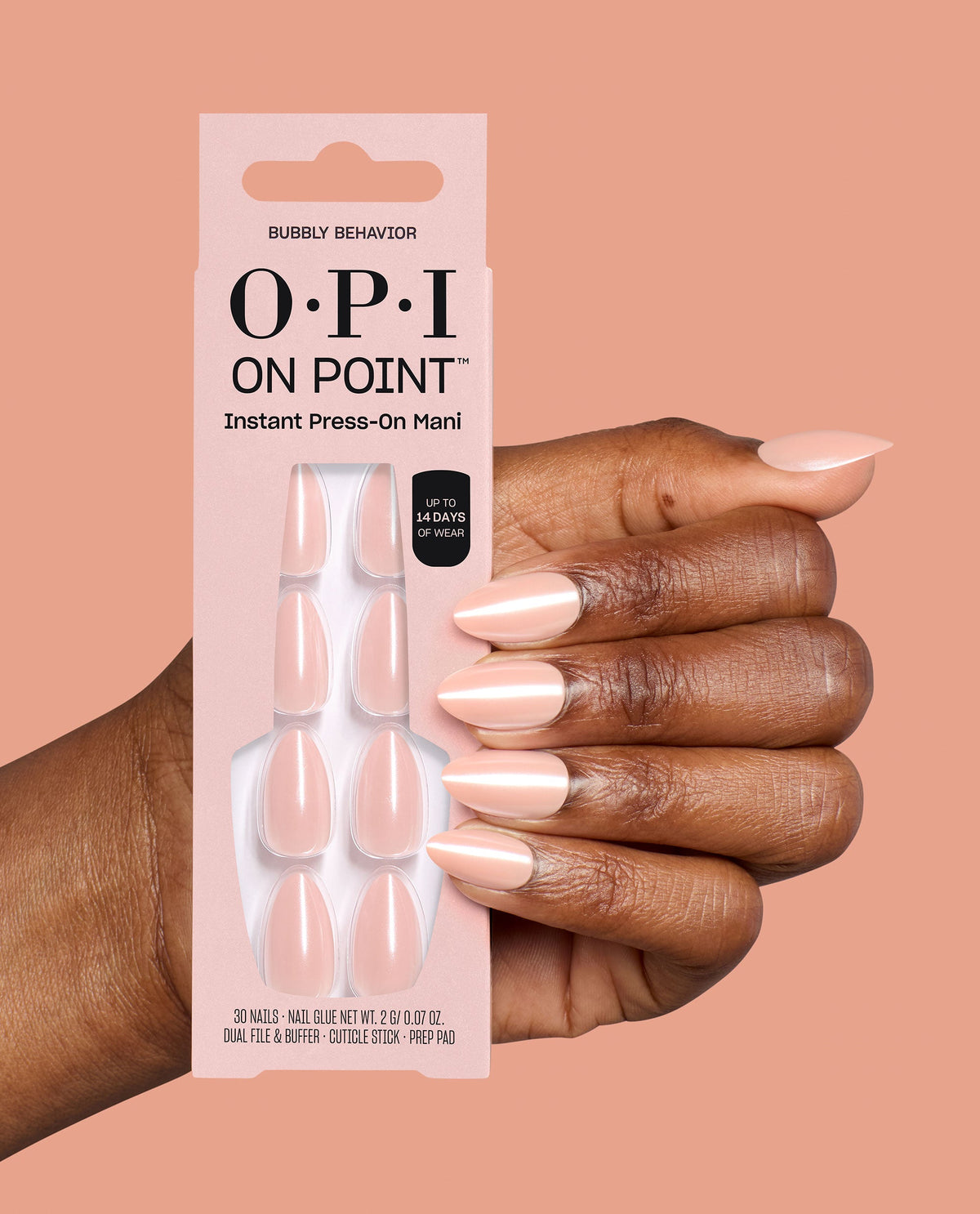 Hand wearing pale pink almond press-on nails holds OPI On Point Bubbly Behavior Instant Press-On Mani packaging, a soft neutral option for fall nail colors on a peach background.