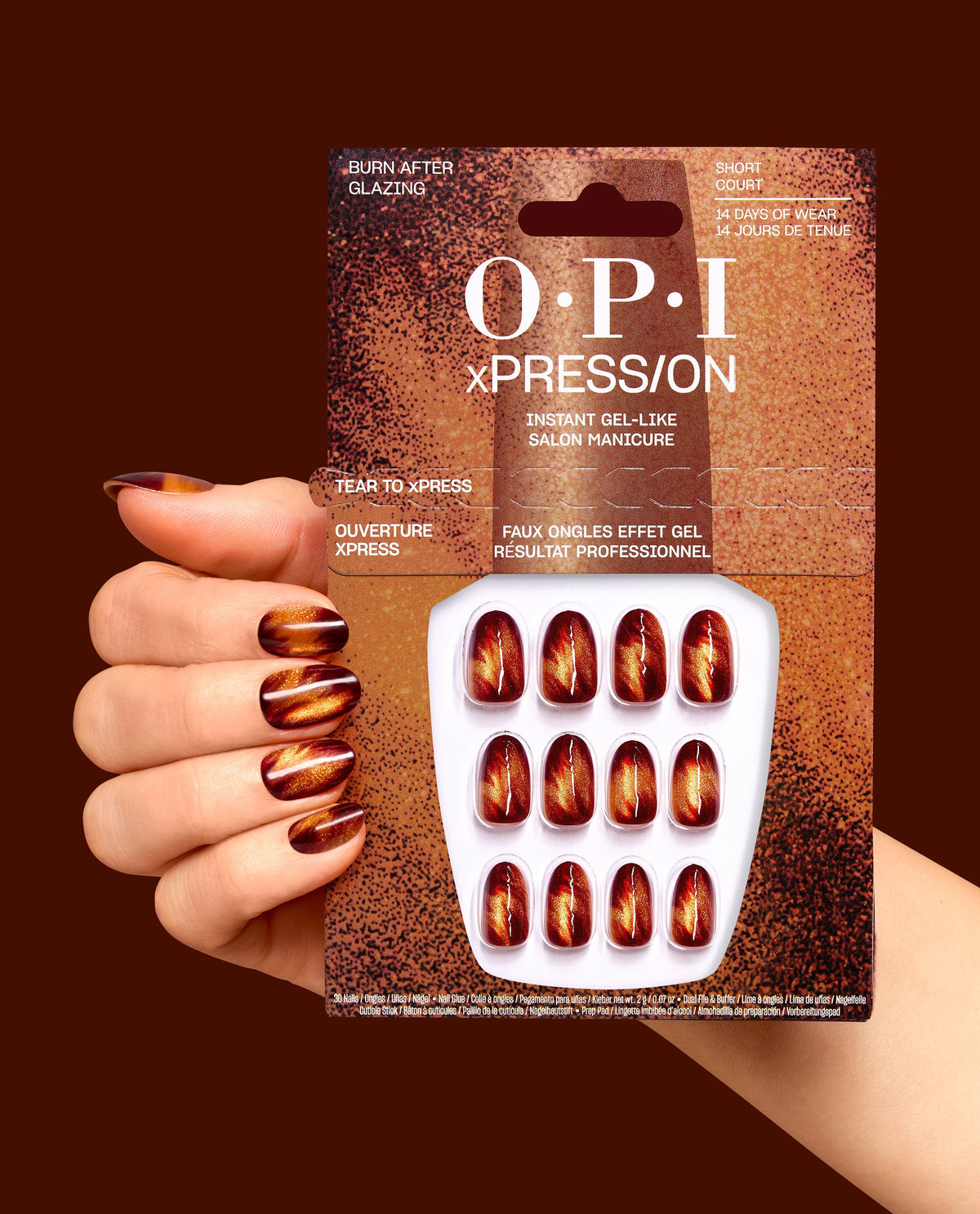 OPI xPRESS/ON Burn After Glazing press-on nails are held beside a matching manicure, showing short court gel-like nails in shimmering red, copper, and amber fall nail colors on a dark brown background.