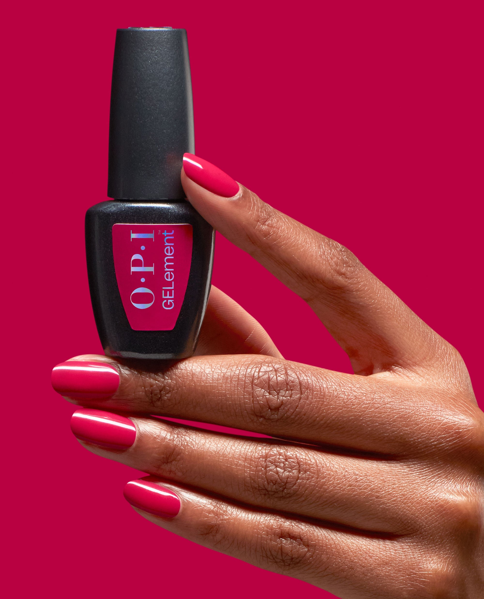 Hand with glossy hot pink Clawberry Margarita at-home gel manicure holds an OPI GELElement bottle against a matching magenta background, showcasing the vibrant OPI nail polish gift set color and smooth salon-quality finish.