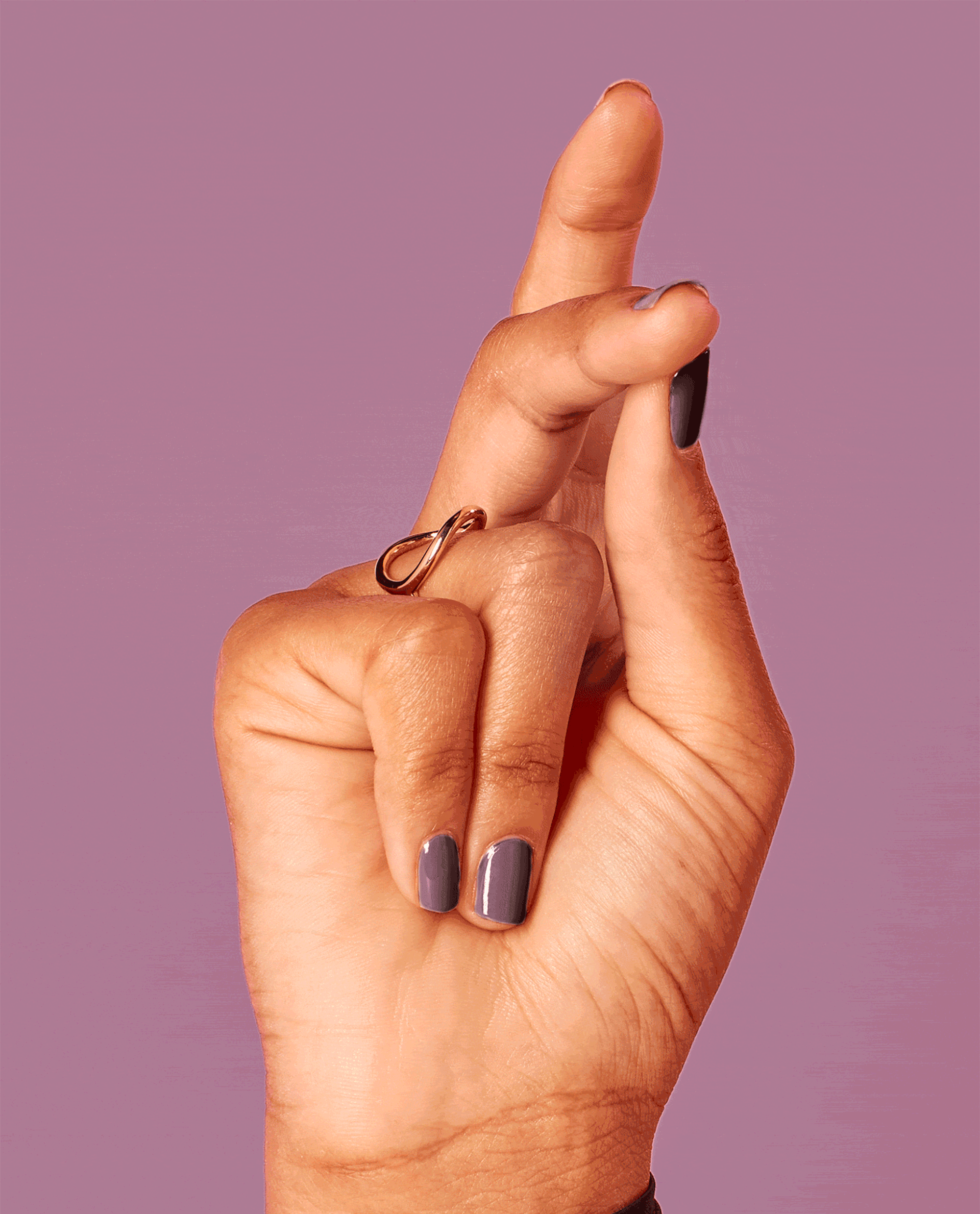 Hand with fingers crossed shows glossy mauve Claydreaming nail lacquer, highlighting OPI nail polish on short, neatly manicured nails against a solid dusty-purple background.