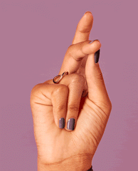 Hand with fingers crossed shows glossy mauve Claydreaming nail lacquer, highlighting OPI nail polish on short, neatly manicured nails against a solid dusty-purple background.