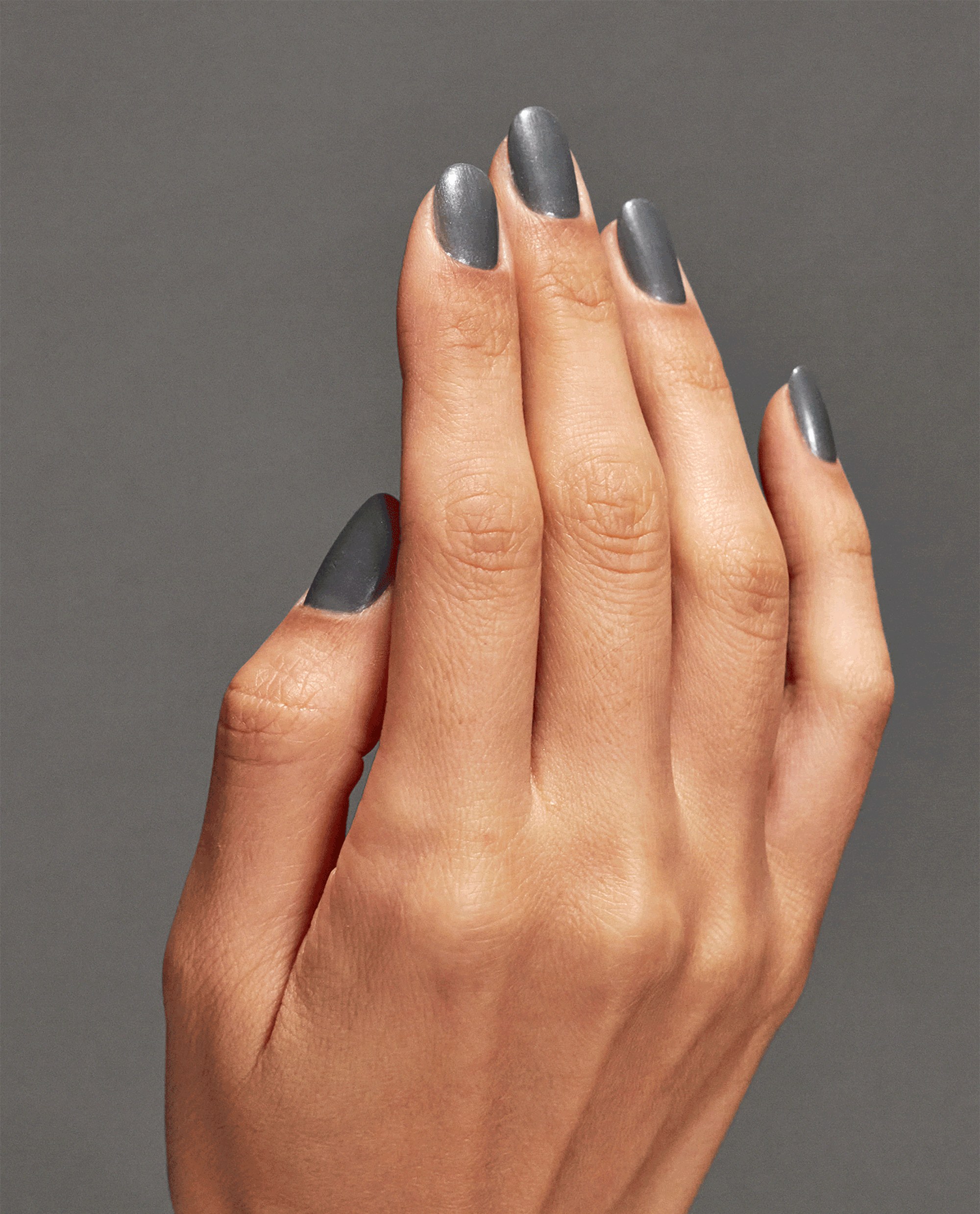Hand with medium skin tone shows neatly manicured nails painted in Clean Slate nail lacquer, a smooth slate-gray OPI nail polish shade, against a matching gray background, highlighting the glossy, opaque coverage and modern neutral color.