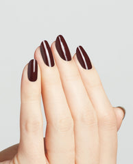 Hand shows long oval nails painted in OPI nail polish Complimentary Wine, a deep burgundy nail lacquer with a glossy finish, against a clean light gray background for a modern salon-quality manicure look.