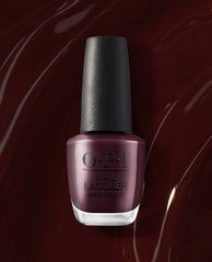 OPI nail polish bottle of Complimentary Wine nail lacquer standing upright, showcasing a deep burgundy-wine shade with a glossy finish against a matching dark red, swirled polish background.