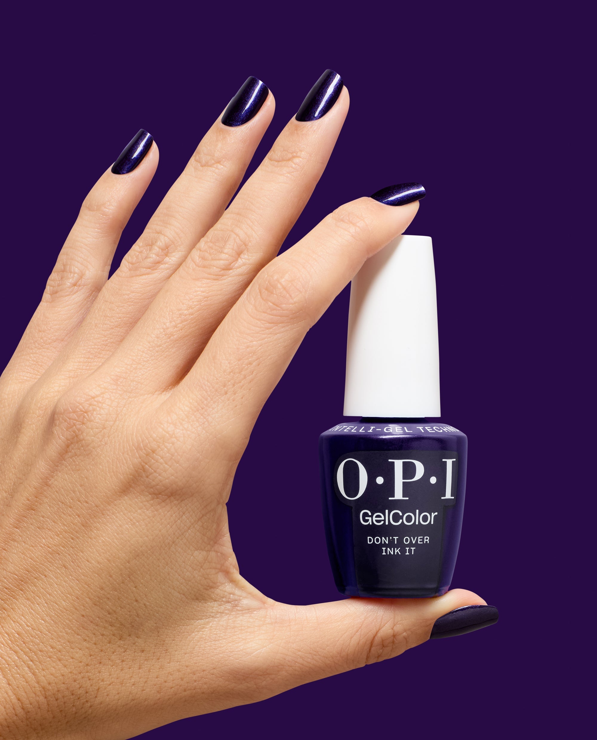 Hand with glossy dark purple shimmer nails holds OPI GelColor Don't Over Ink It gel nail polish bottle against a deep purple background, showcasing bold fall nail colors.