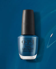 OPI nail polish bottle of Duomo Days, Isola Nights nail lacquer standing upright, showcasing a rich deep teal-blue shade with a black textured cap against a glossy matching blue background.
